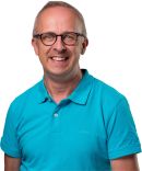 Herr Schütz trägt eine Brille und ein blaues Shirt. Er lächelt freundlich.