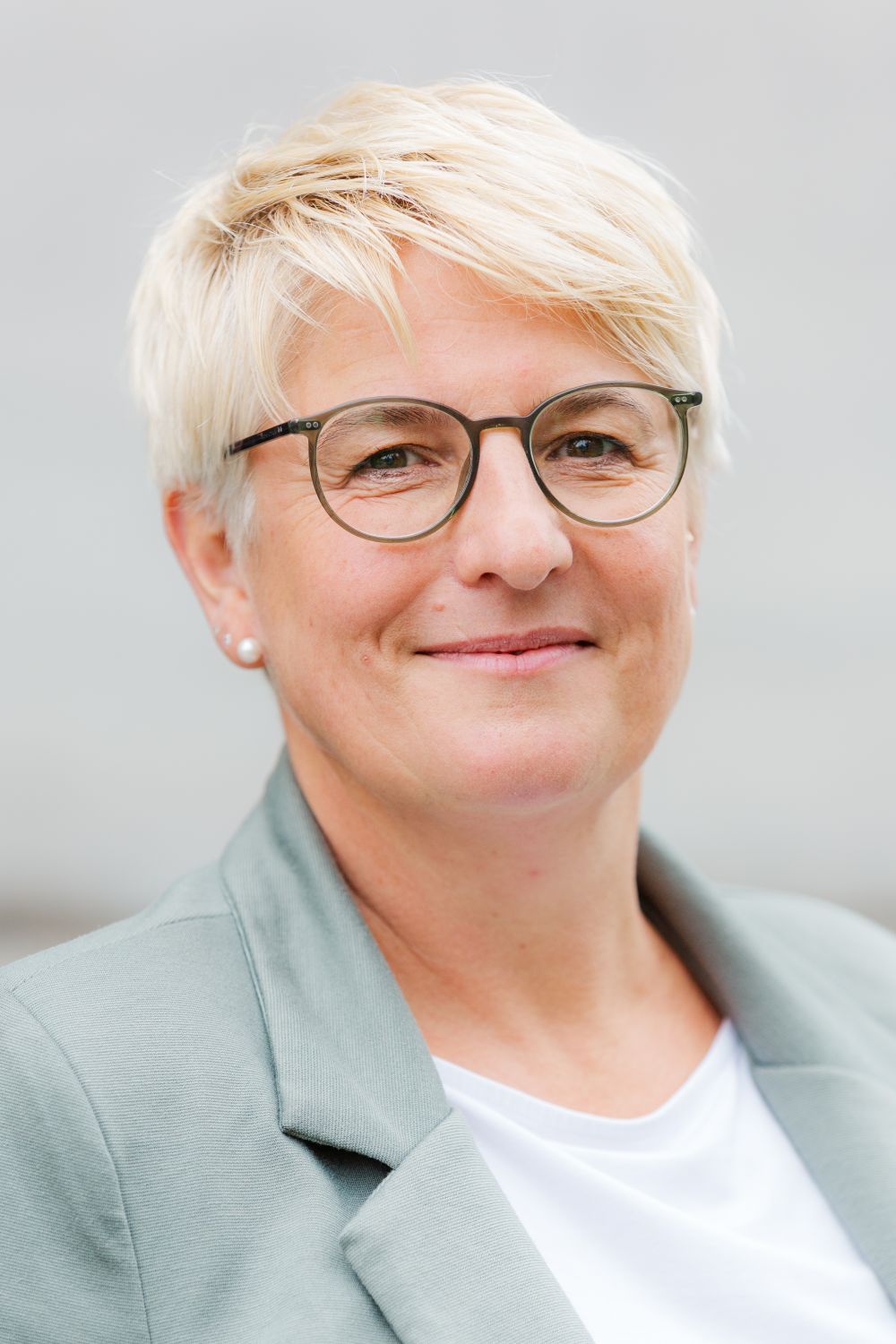 Frau Rösch trägt kurze, blonde Haare und eine Brille. Sie lächelt freundlich.