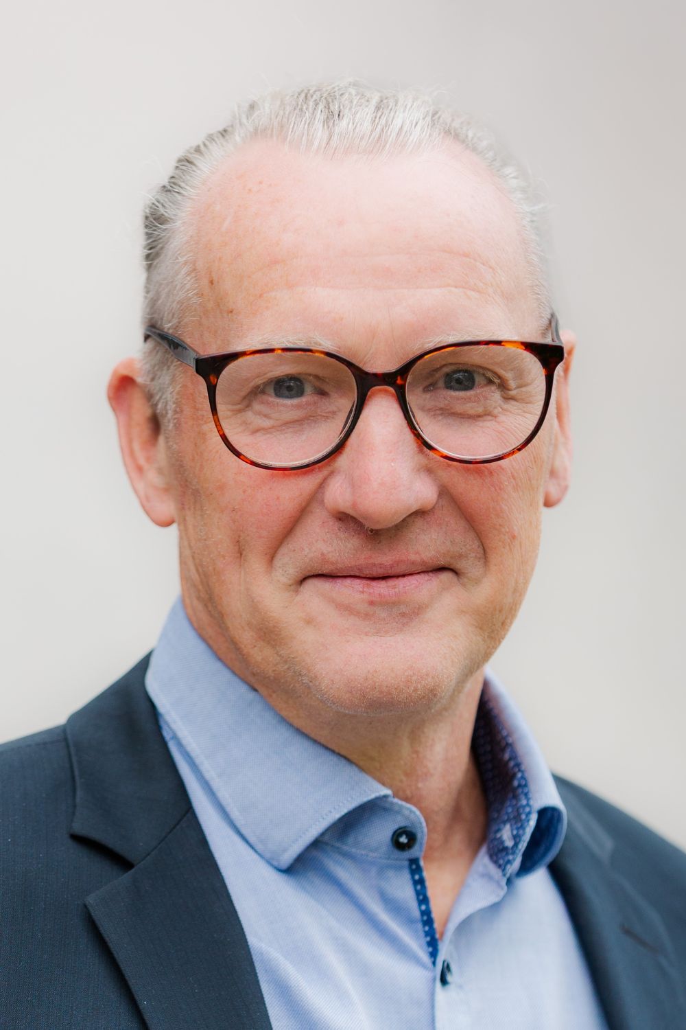 Das Bild zeigt Herrn Schneider. Er trägt halblange, graue Haar und einen Zopf. Er trägt eine Brille und lächelt freundlich.