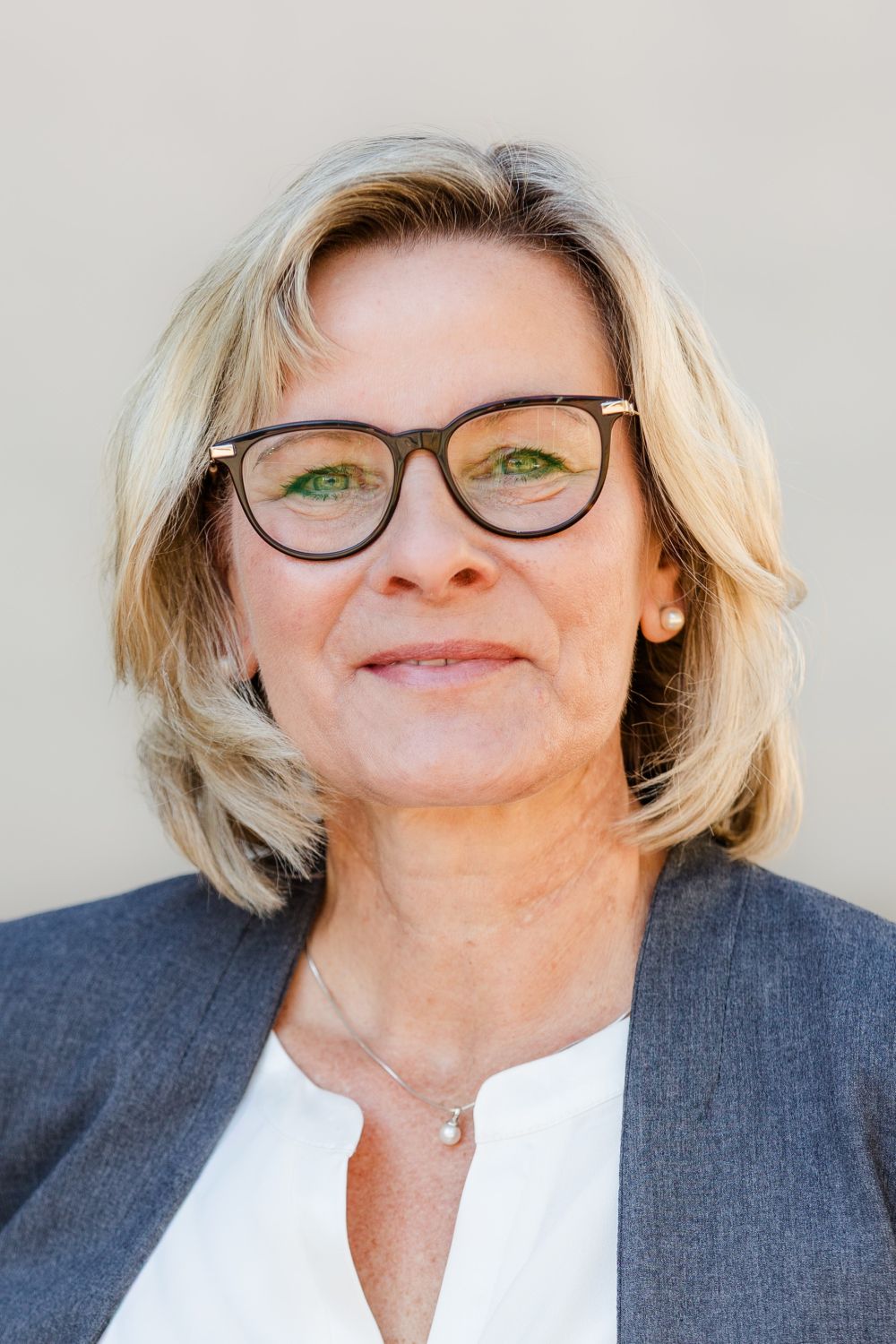 Frau Schreiber trägt halblange, blonde Haare und eine Brille. Sie lächelt freundlich.